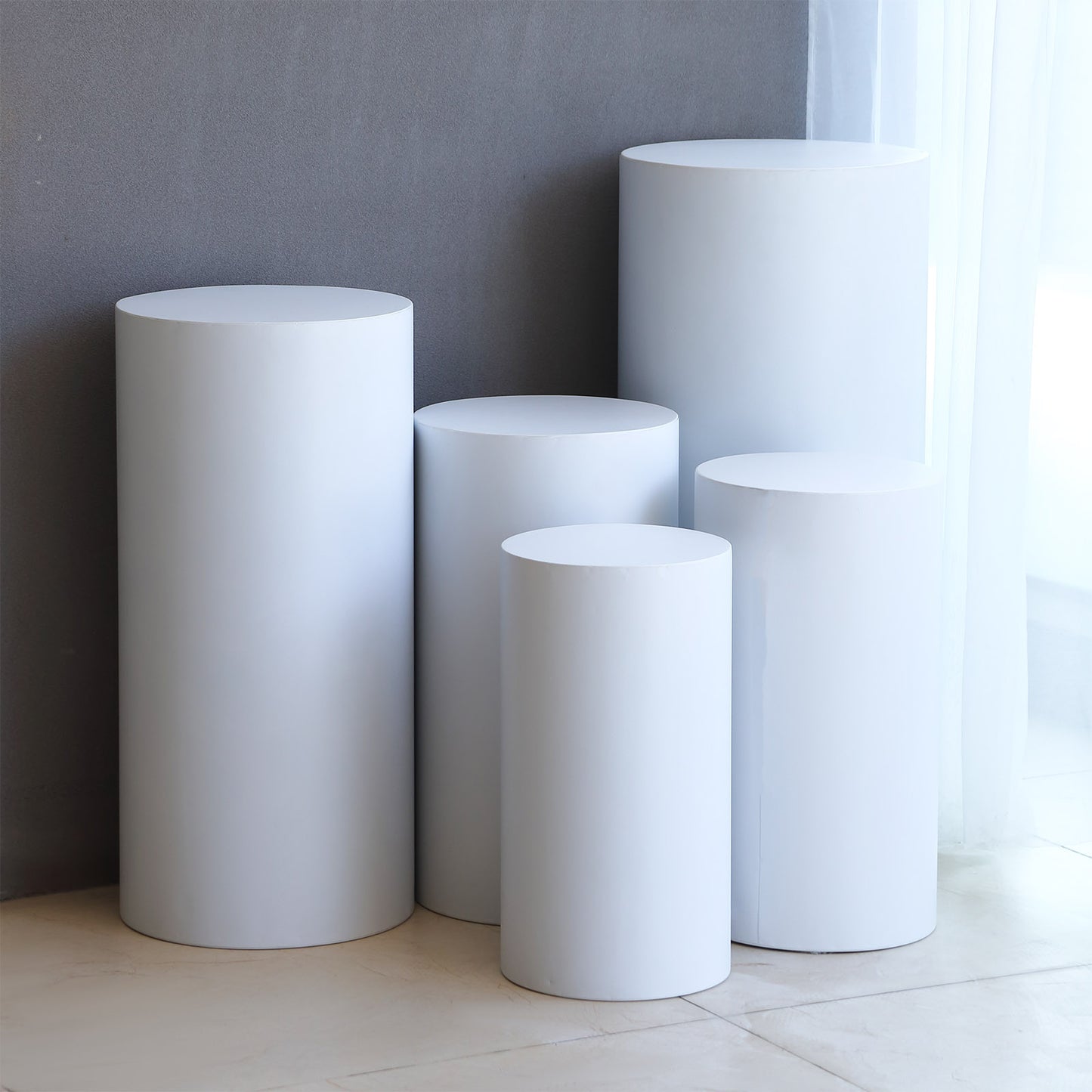 Set of 5 white metal cylinder pillar stands for wedding display.