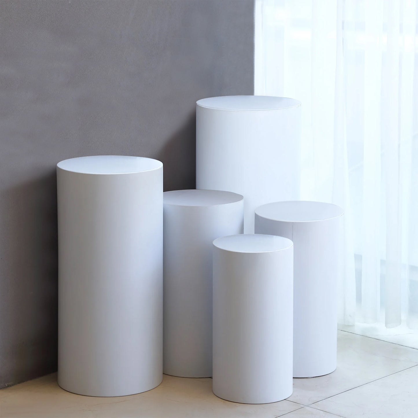 Set of 5 white metal cylinder pillar stands for wedding displays.
