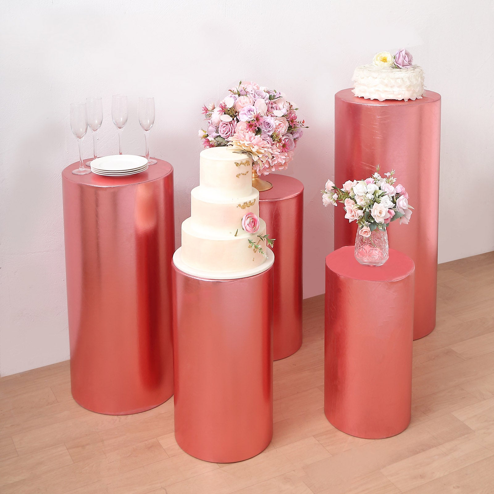 Metallic rose gold pedestal stand covers on display with floral arrangements and cake.