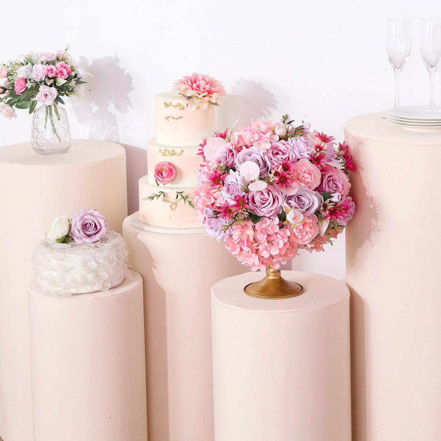 Blush spandex pedestal stand covers on cylindrical stands with floral arrangements.
