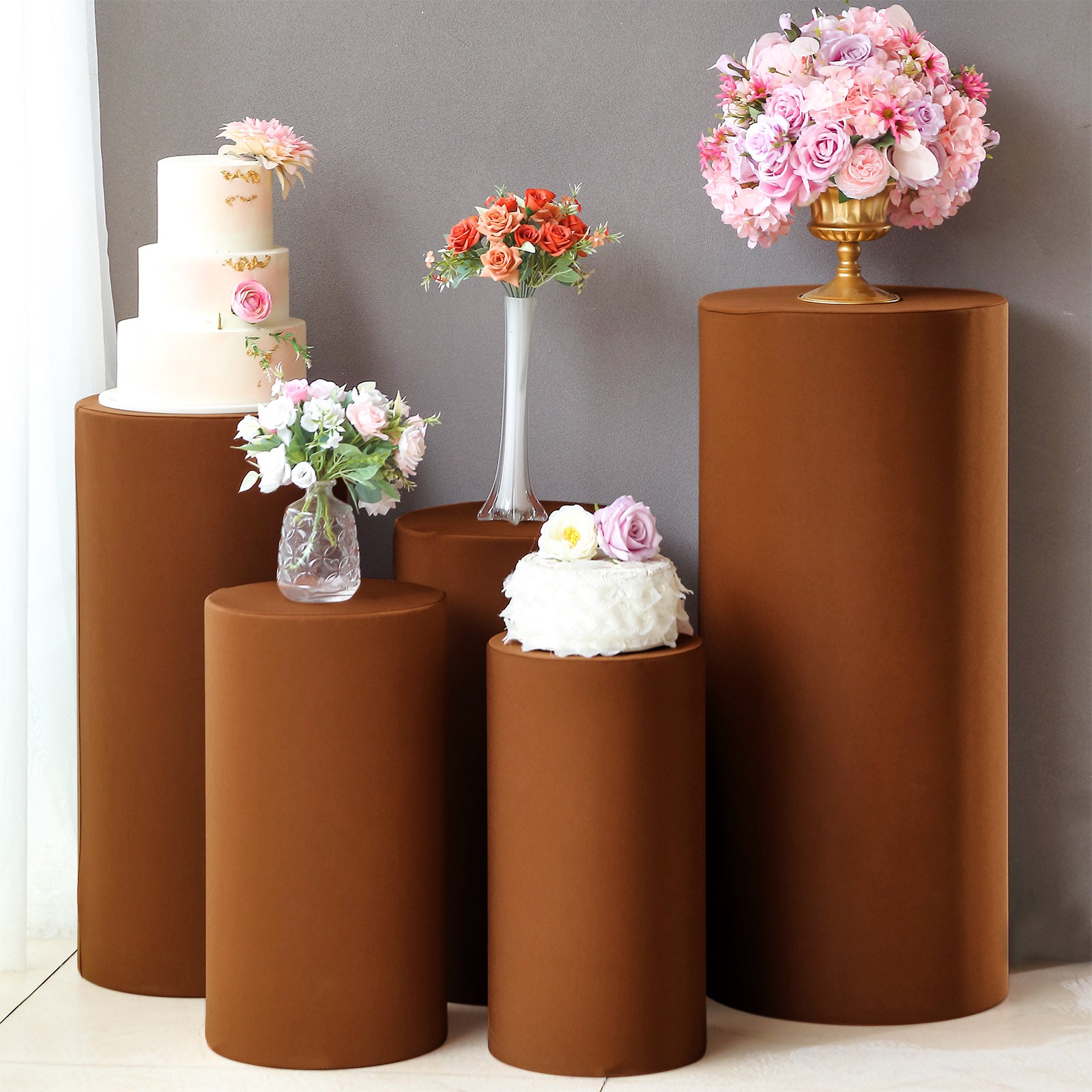 Cinnamon brown spandex pedestal stand covers with floral arrangements on top.