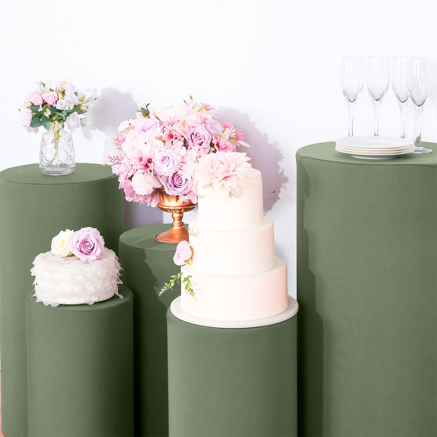 Dusty sage green spandex pedestal stand covers with floral decor and cake.