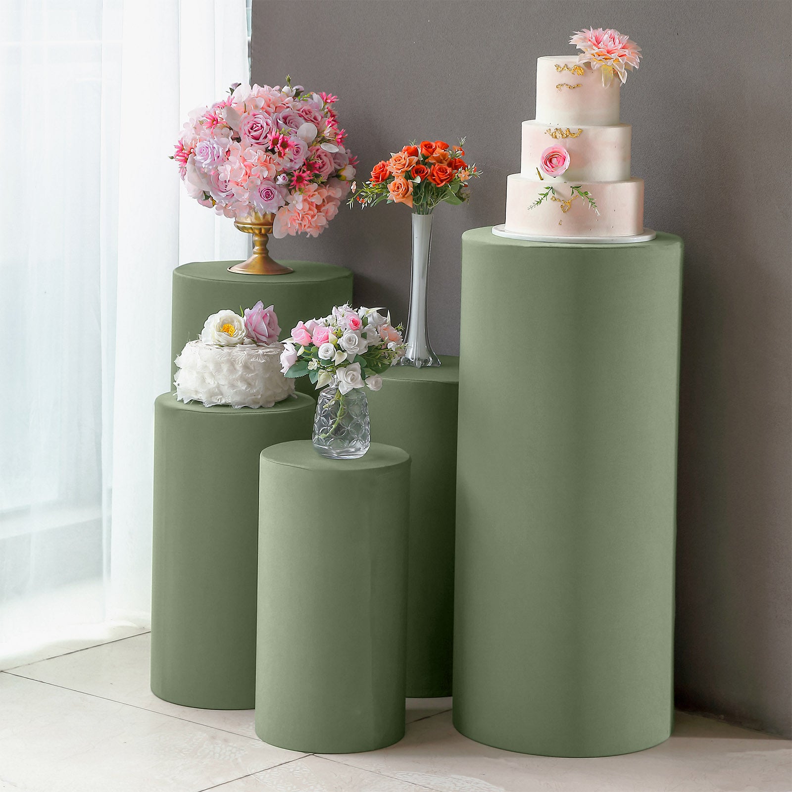 Dusty sage green spandex pedestal stand covers with floral arrangements.
