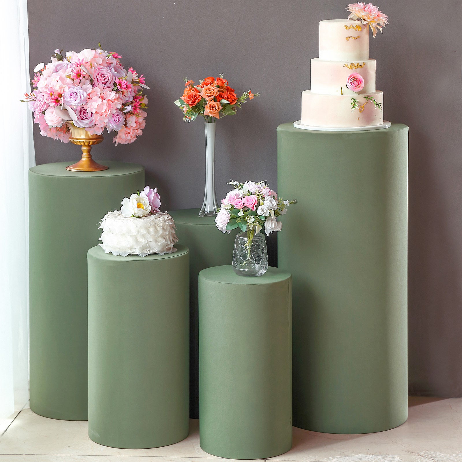 Dusty sage green spandex cylinder pedestal stand covers with floral arrangements.
