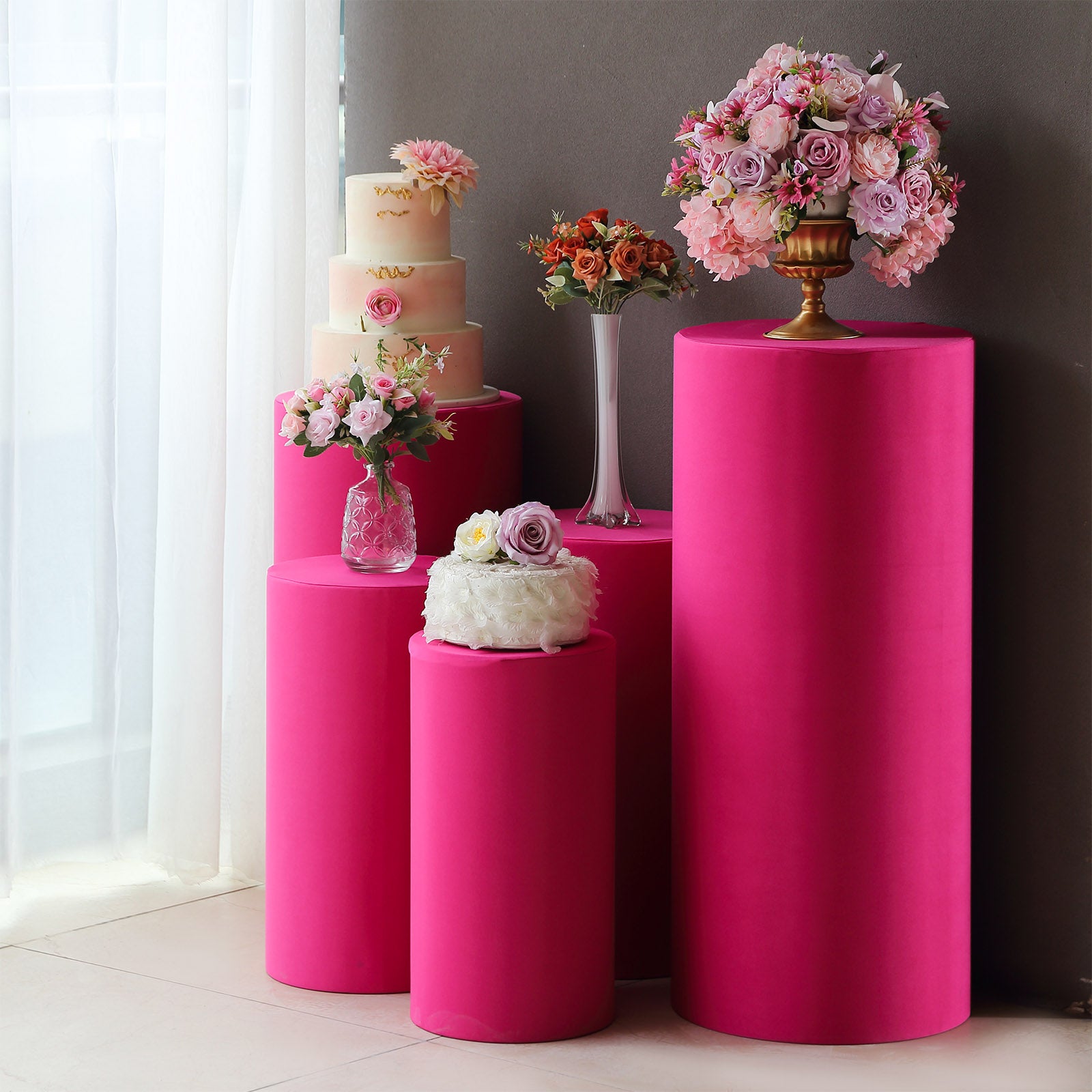 Fuchsia spandex pedestal stand covers with floral arrangements on top.