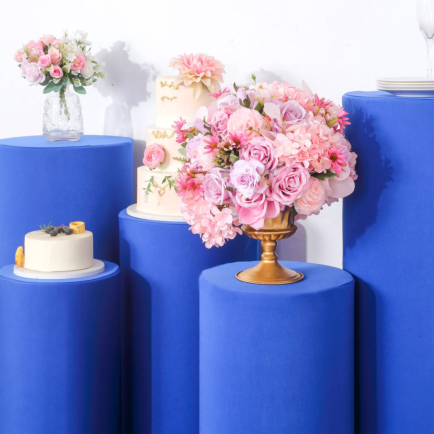 Royal blue spandex pedestal stand covers with floral arrangements on top.