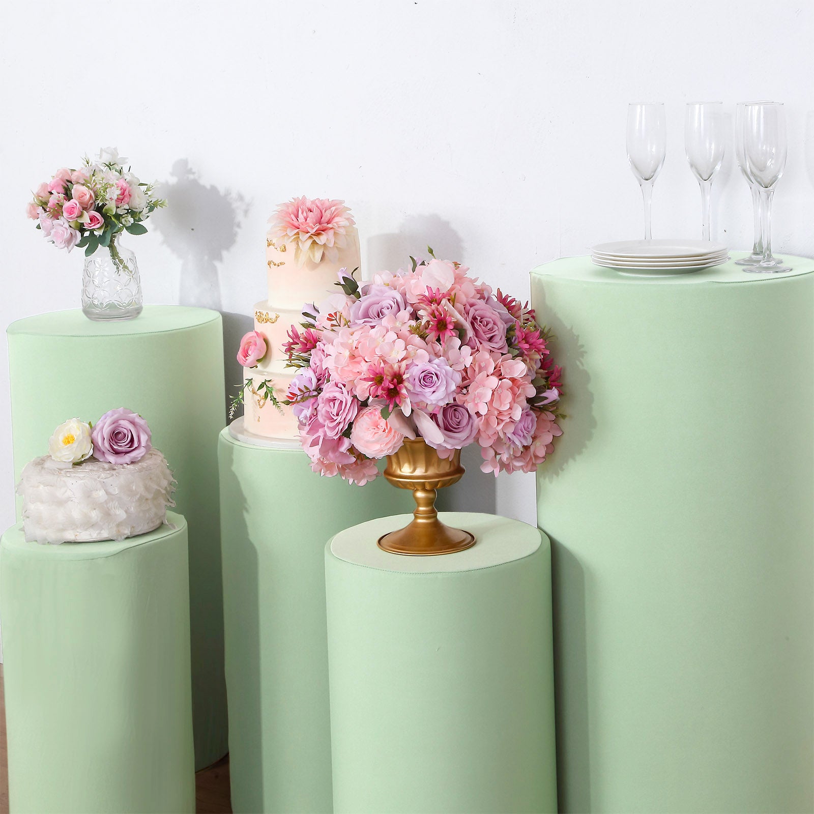 Sage green spandex covers on cylinder pedestal stands with floral arrangements.
