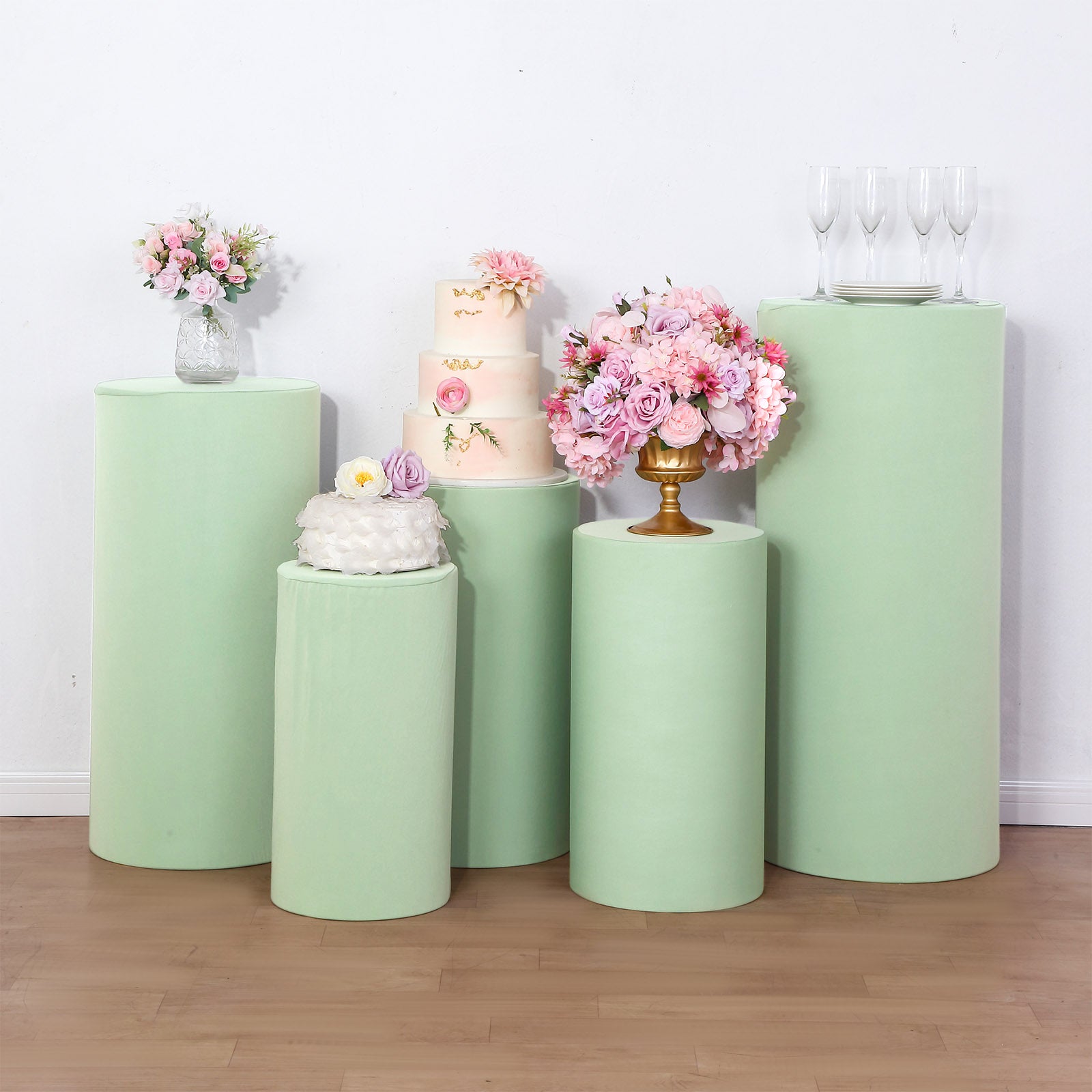 Sage green spandex pedestal stand covers with floral and cake decorations.