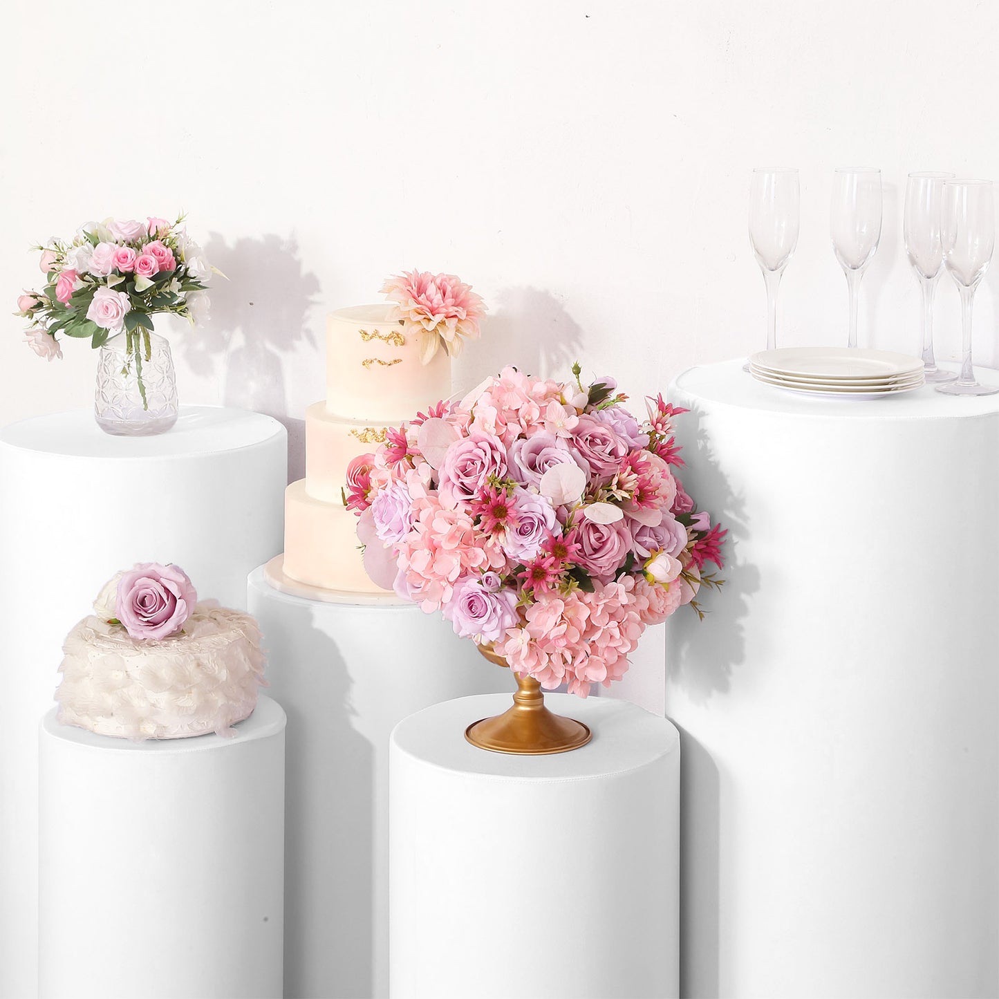 White stretchable pedestal stand covers on display with floral arrangements and cake.