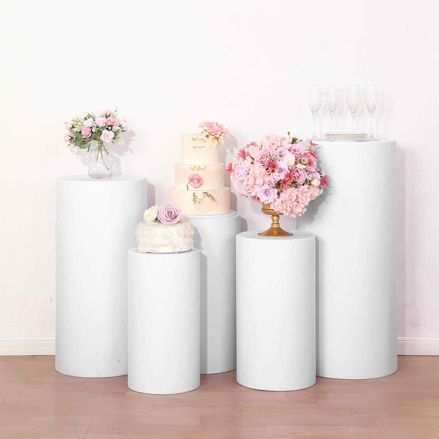 White spandex pedestal stand covers on display with floral arrangements and a cake.