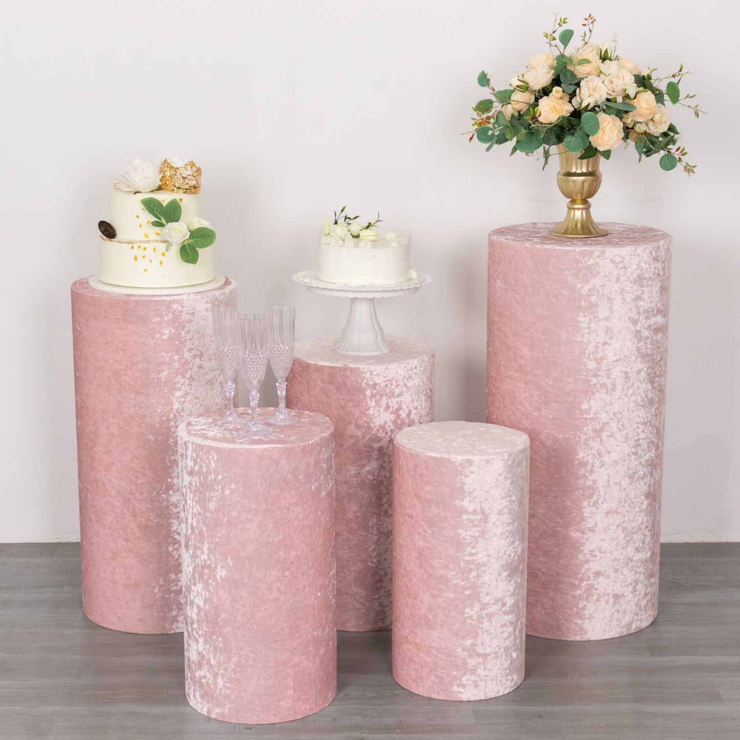 Blush crushed velvet pedestal stand covers set with decorative flowers and cakes.