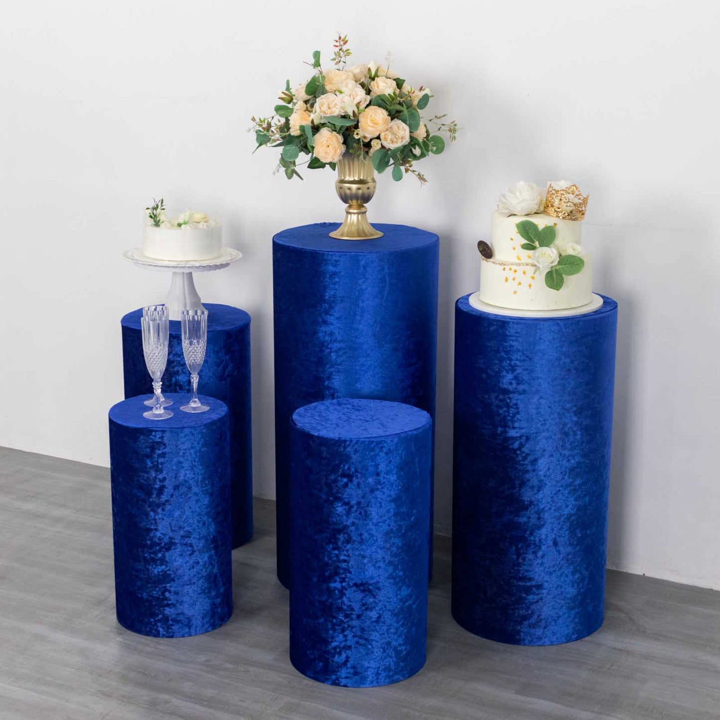 Royal blue crushed velvet pedestal stand covers with floral arrangements and cakes.