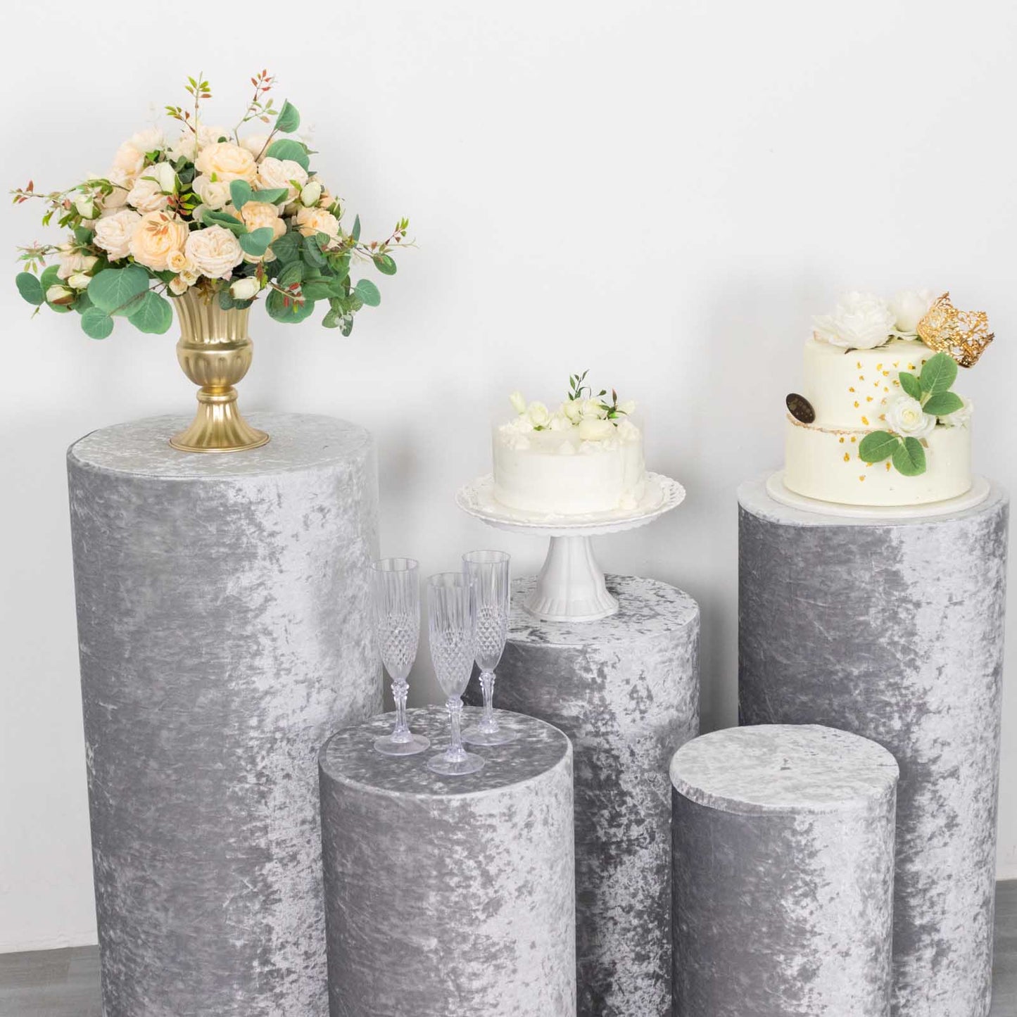 Silver crushed velvet pedestal stand covers with floral arrangements and cakes.