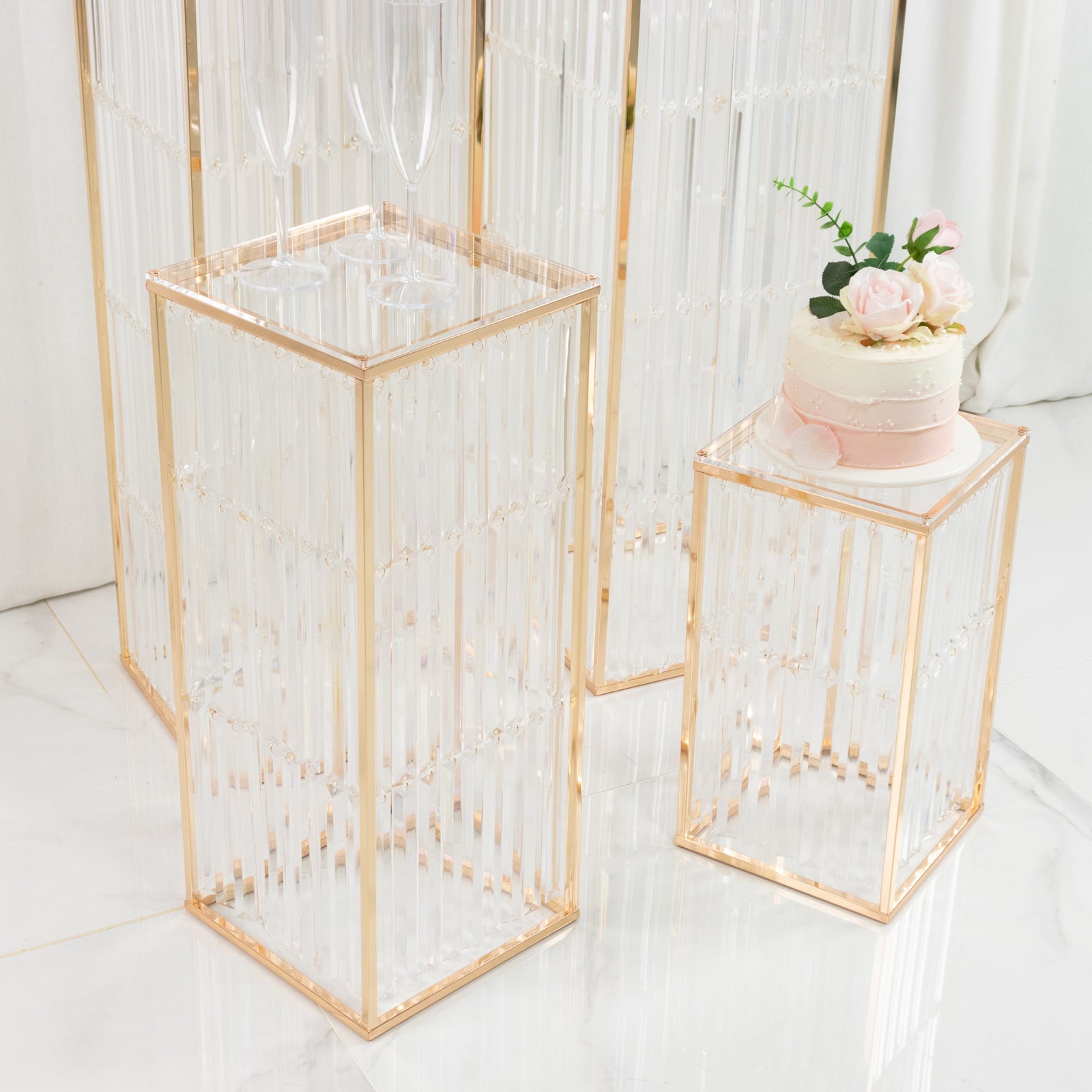Gold pedestal stands with acrylic tops and crystal pendant chains.