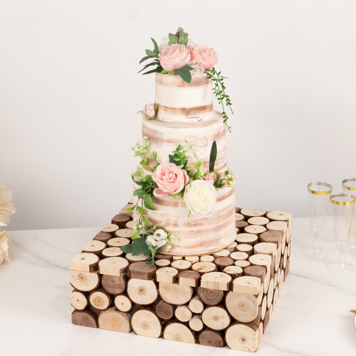 Natural wooden square pedestal riser for cake display with floral accents.