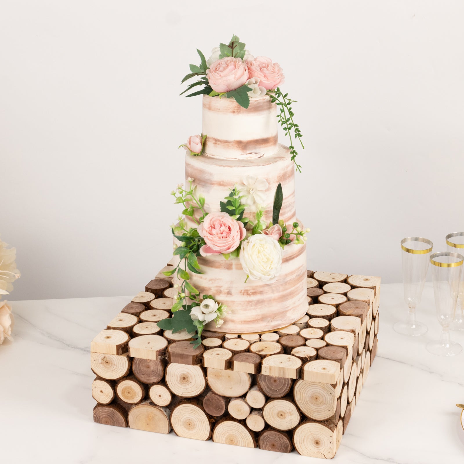 Natural wooden square pedestal riser for cake display with floral accents.