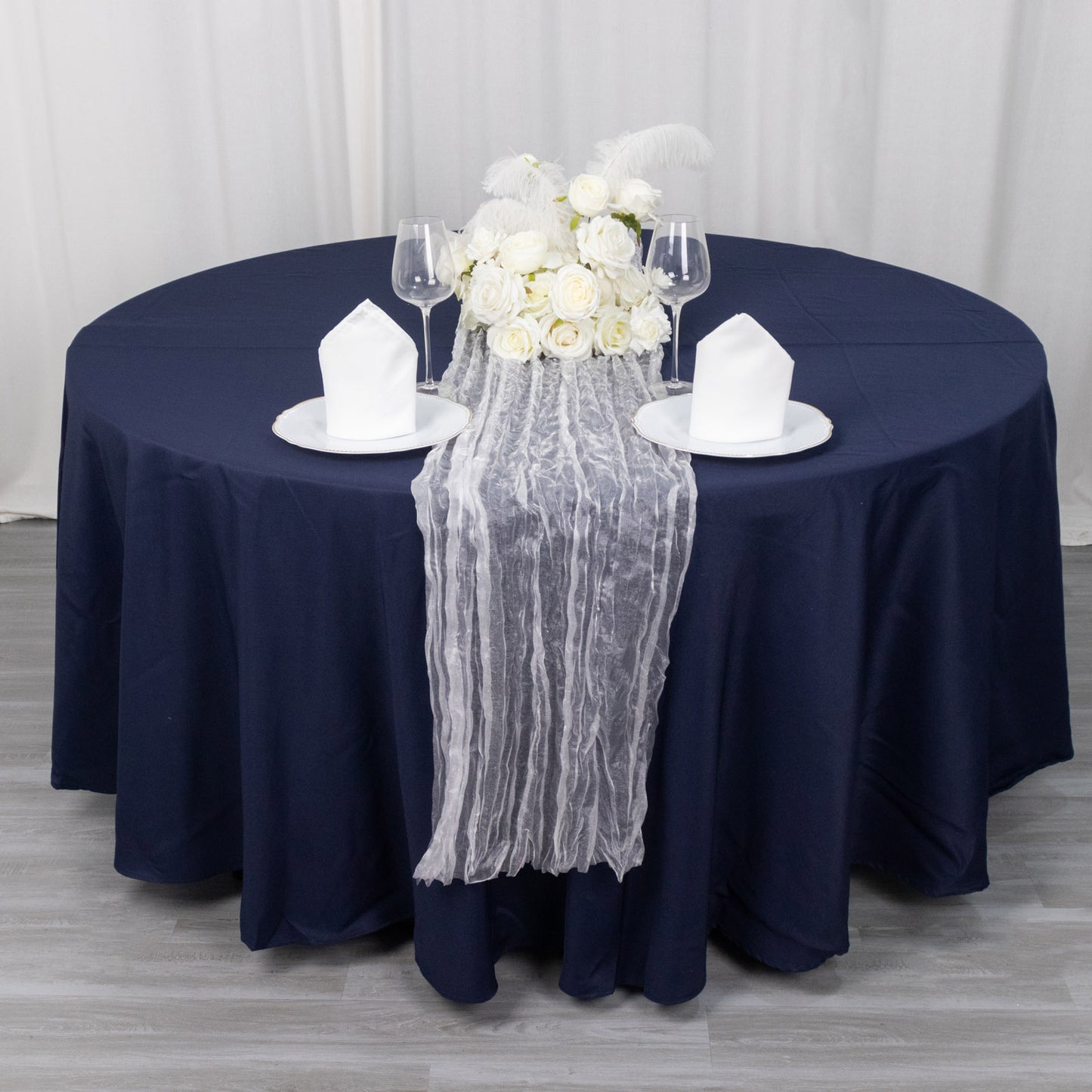 9ft sheer crinkled organza table runner in white on a navy blue table.