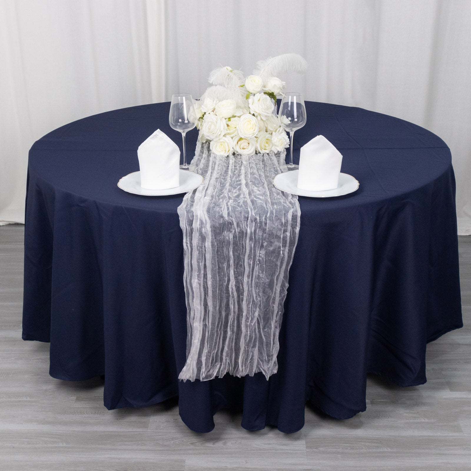 9ft sheer crinkled organza table runner in white on a navy blue table.