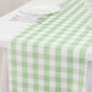 14"x108" White Sage Green Gingham Table Runner on a white table.