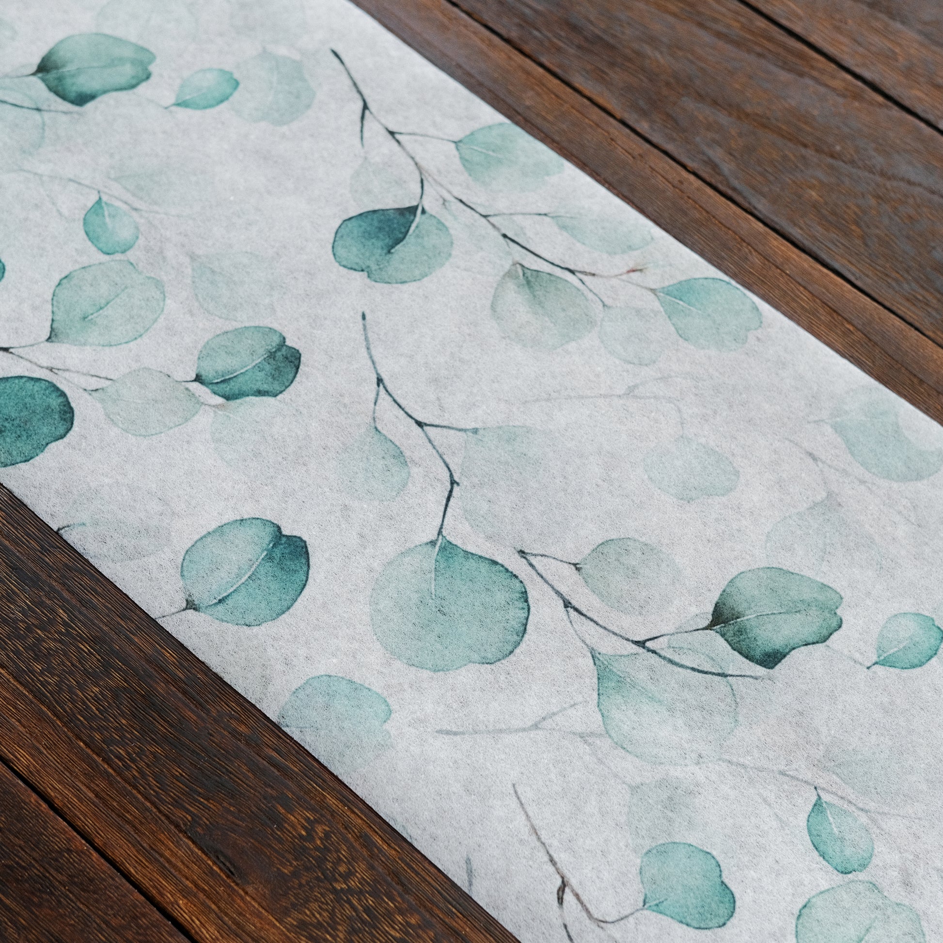 White disposable table runner with green eucalyptus leaves print.