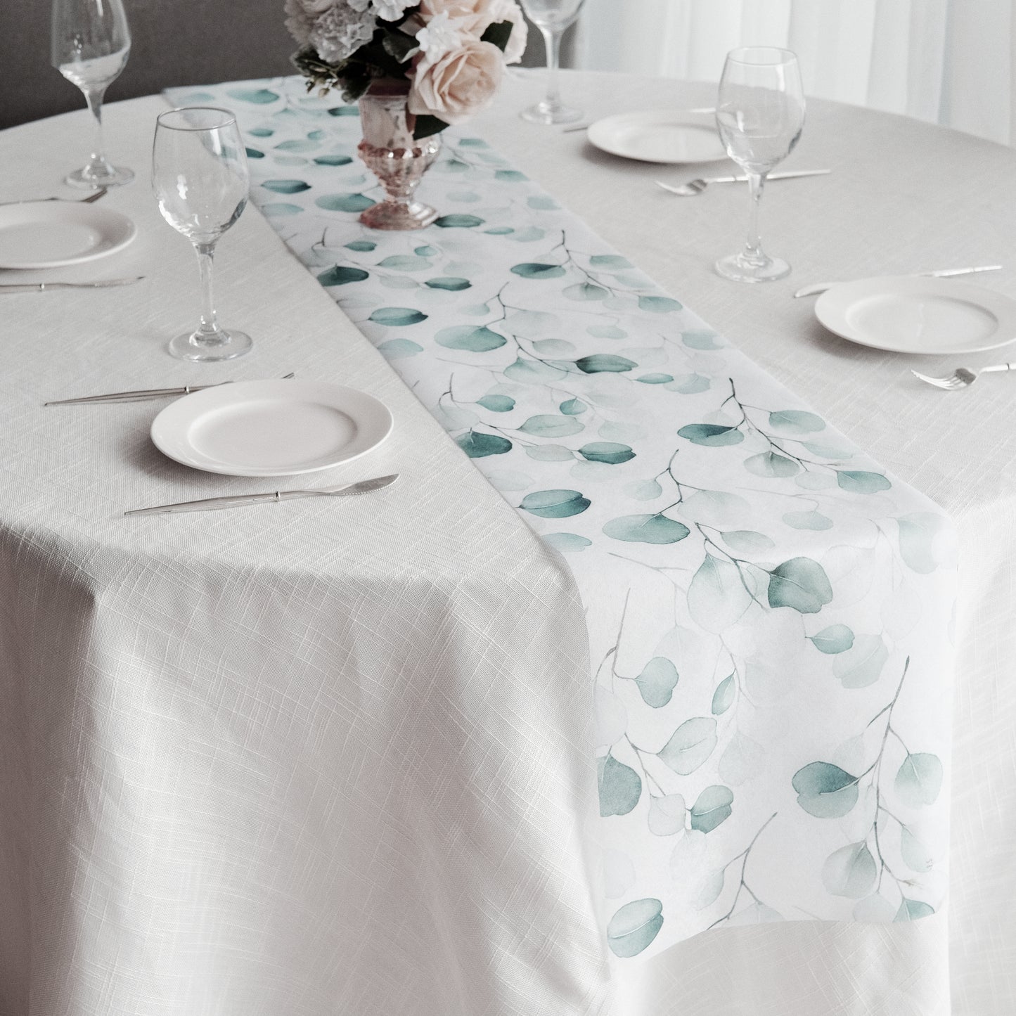 White disposable table runner with green eucalyptus leaves print on a dining table.