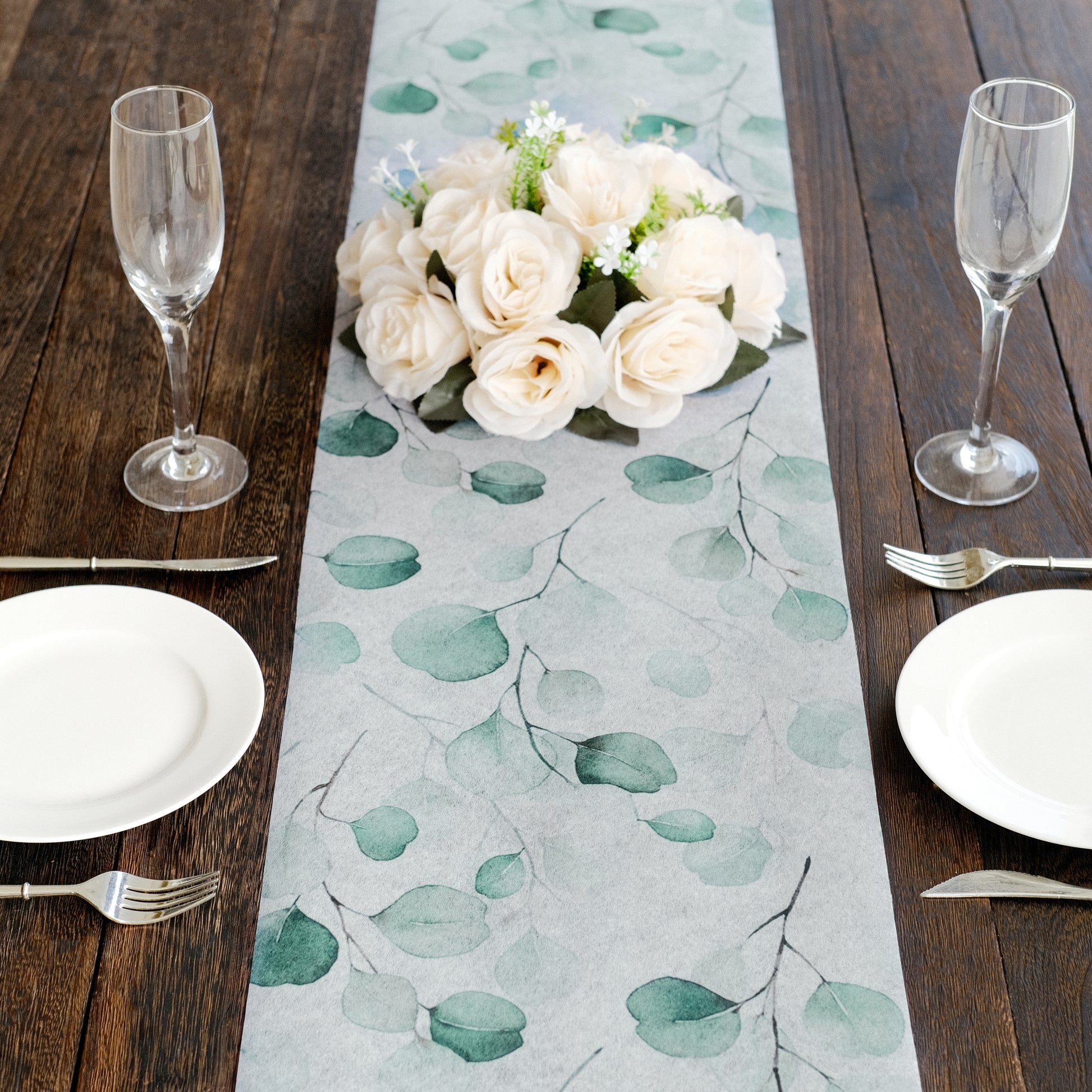 White table runner with green eucalyptus leaves on a wooden table setting.