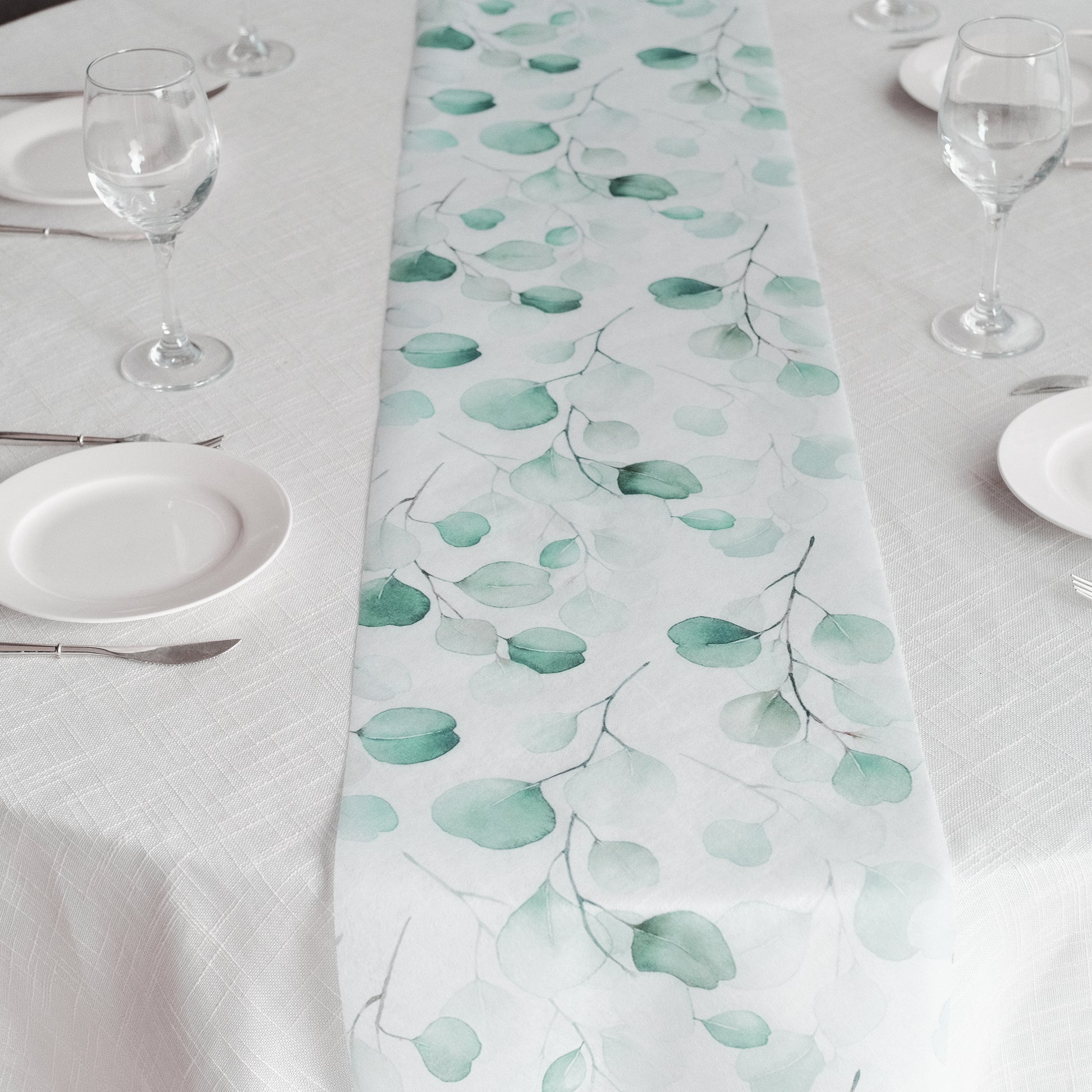 White table runner with green eucalyptus leaves print for stylish dining decor.