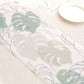 White disposable table runner with green monstera palm leaves print.