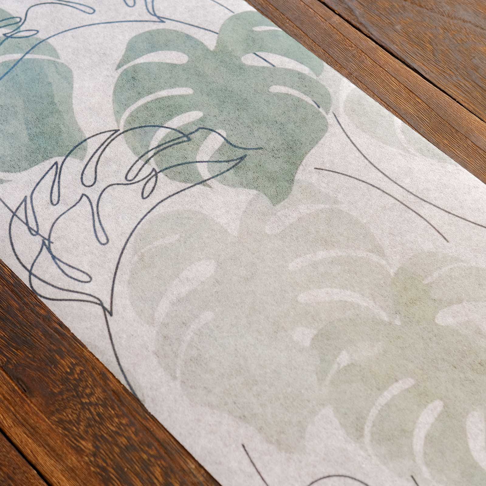 White table runner with green monstera palm leaves print on a wooden table.