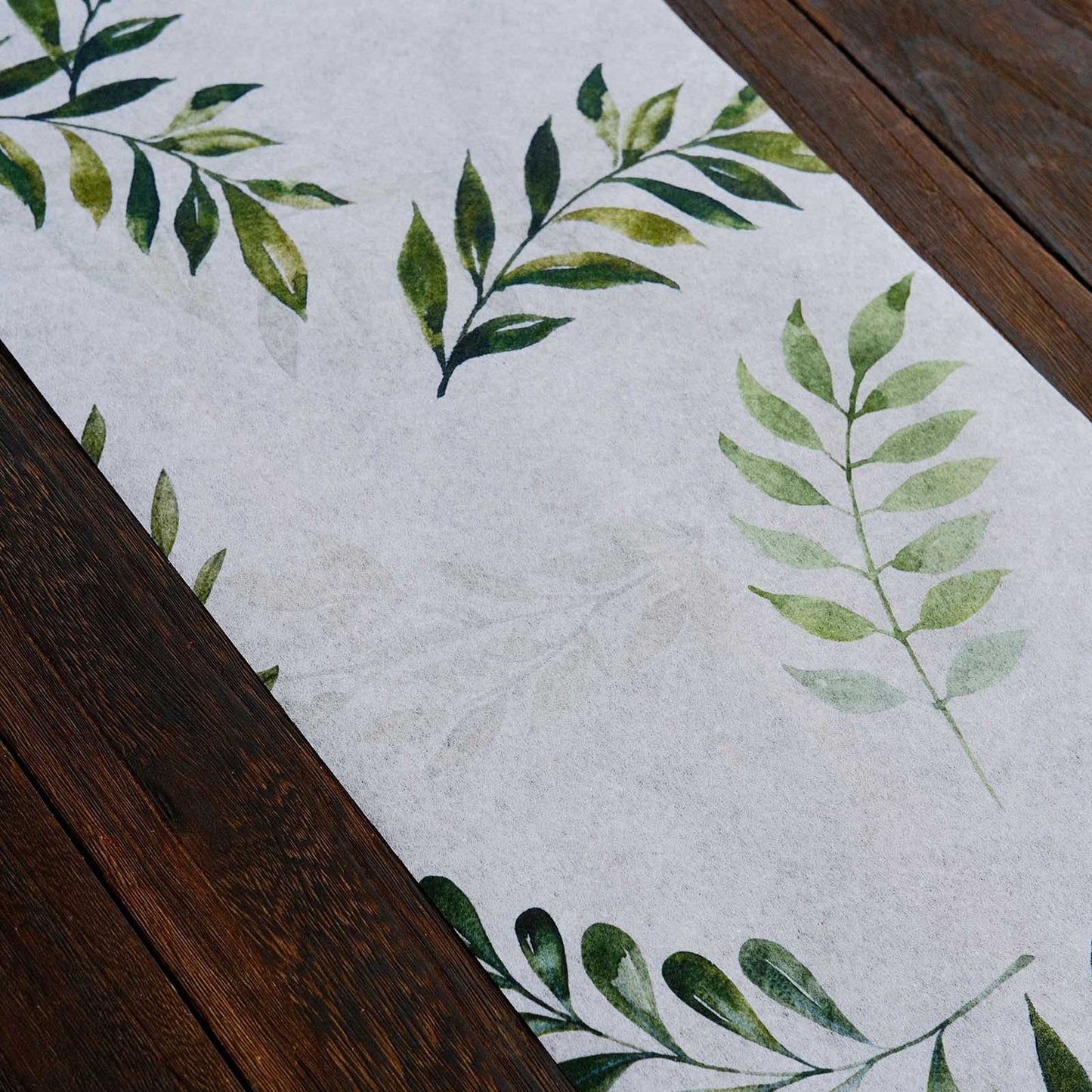 White table runner with green olive leaves print on a wooden surface.