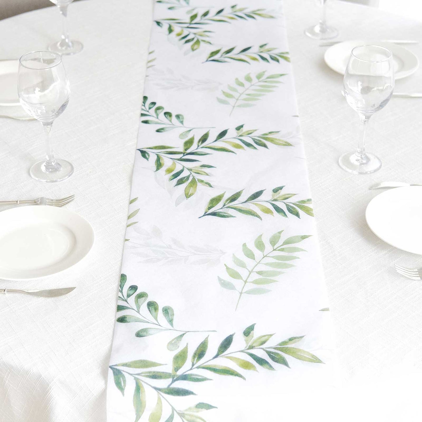 White table runner with green olive leaves print on a dining table setting.