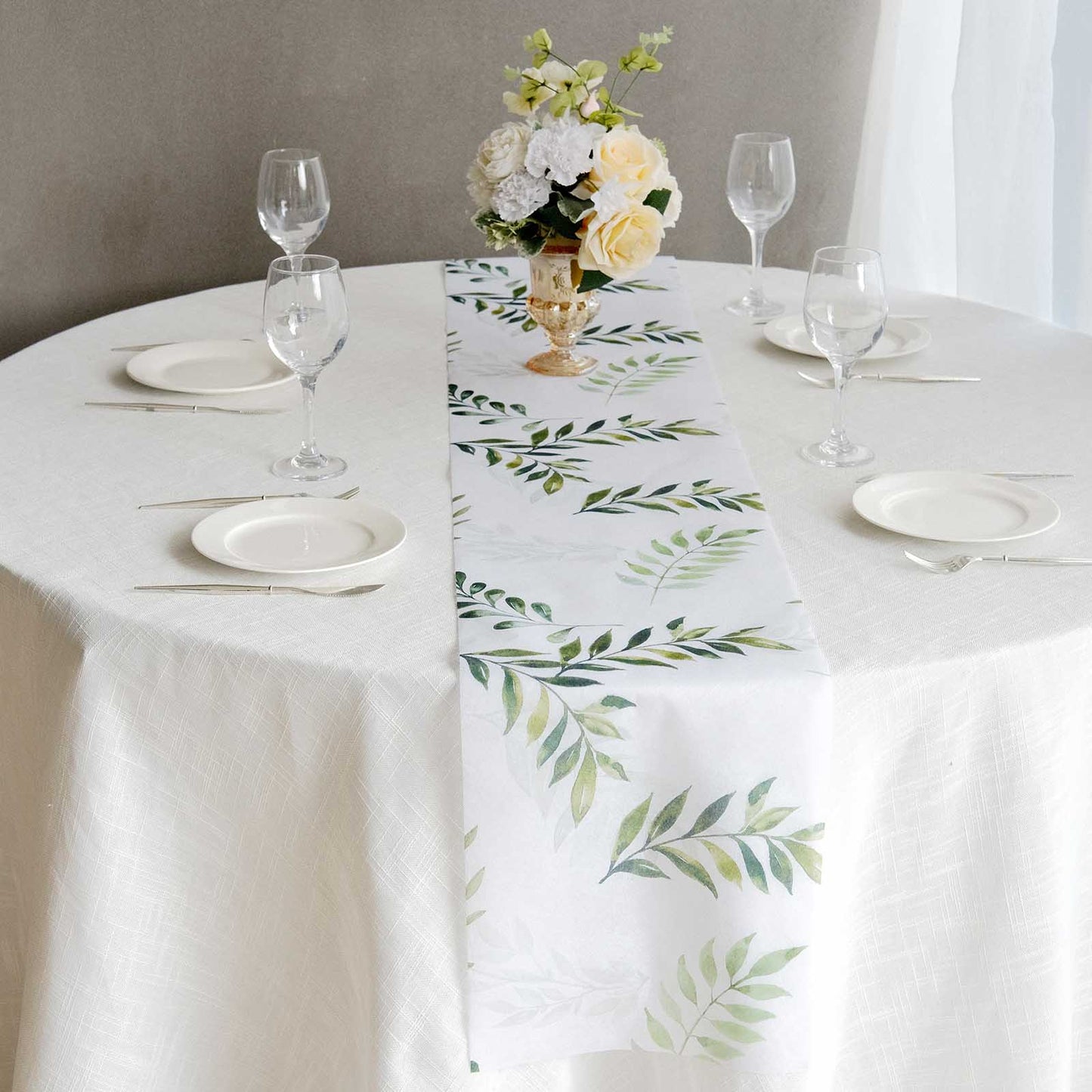 White table runner with green olive leaves print on a dining table setting.