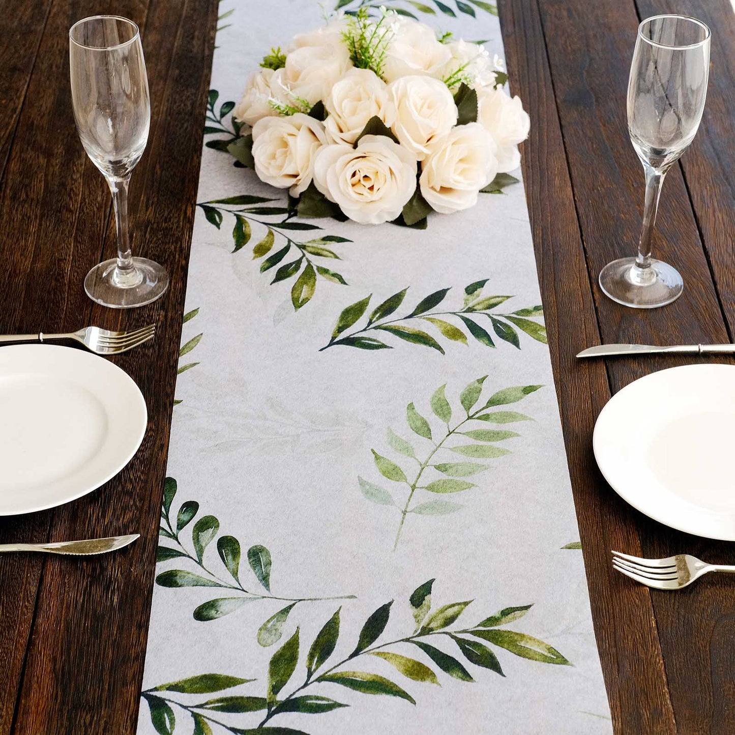 White disposable table runner with green olive leaves print on a wooden table setting.
