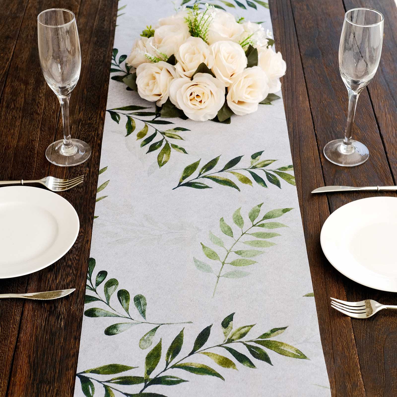 White disposable table runner with green olive leaves print on a wooden table setting.