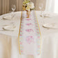 White table runner with pink peony floral print on a dining table setting.