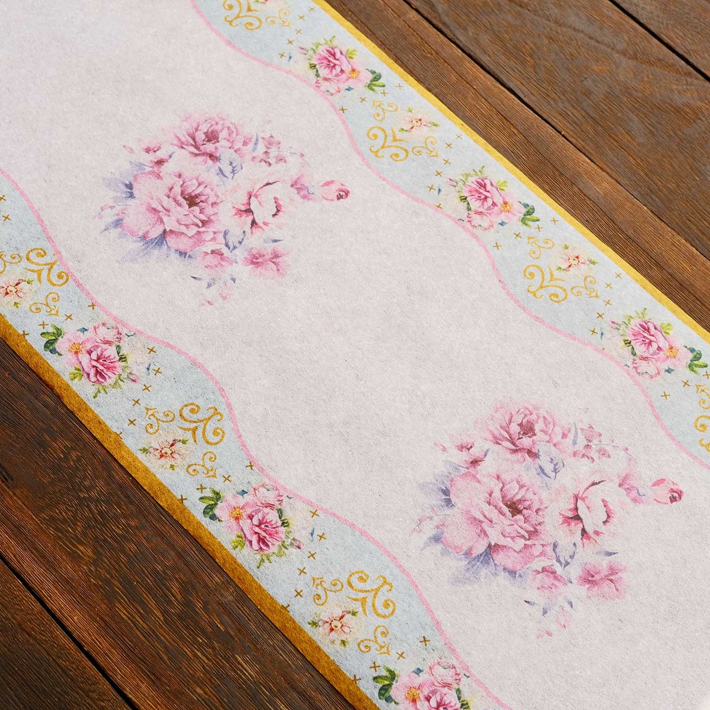 White disposable table runner with pink peony floral print on a wooden table.