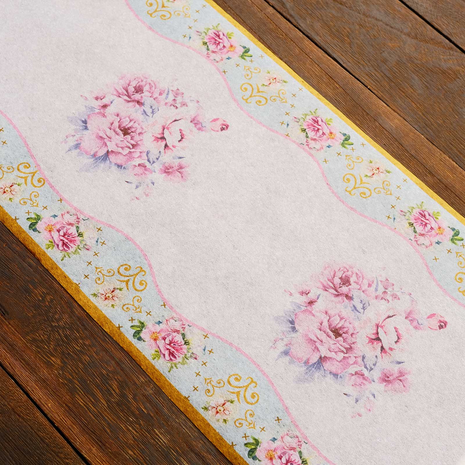 White disposable table runner with pink peony floral print on a wooden table.