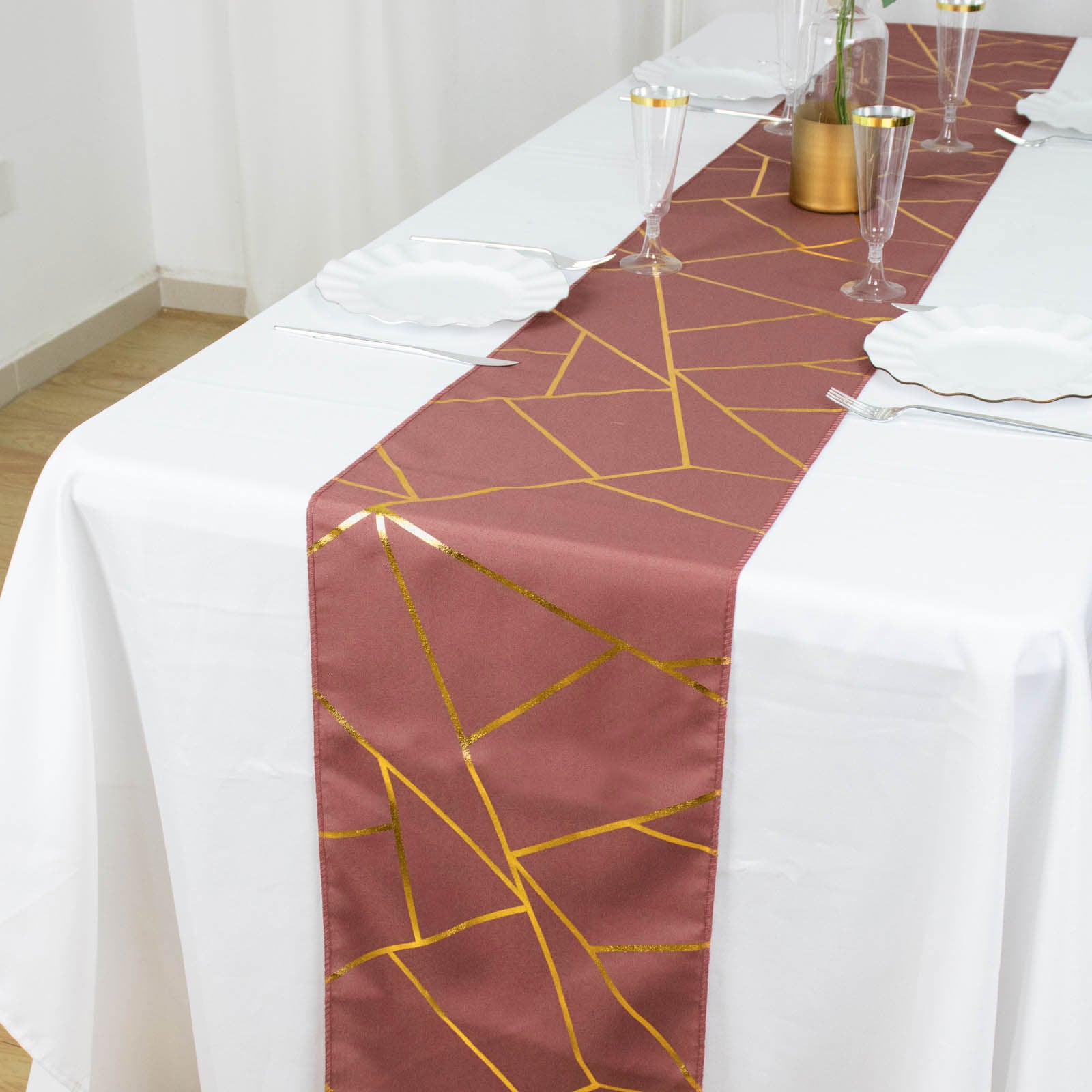 Cinnamon rose table runner with gold foil geometric pattern on a white table.
