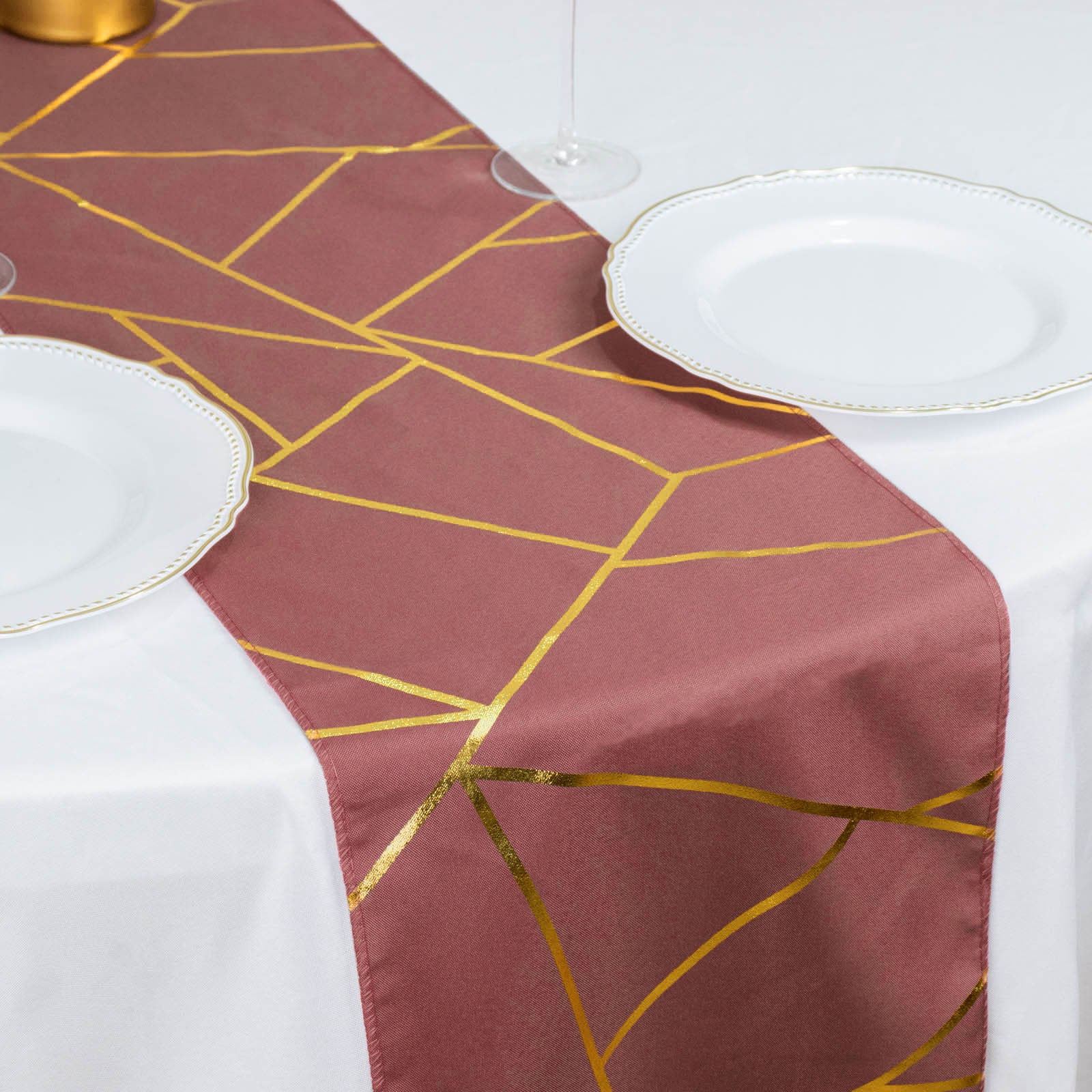 Cinnamon rose table runner with gold geometric pattern on white table.