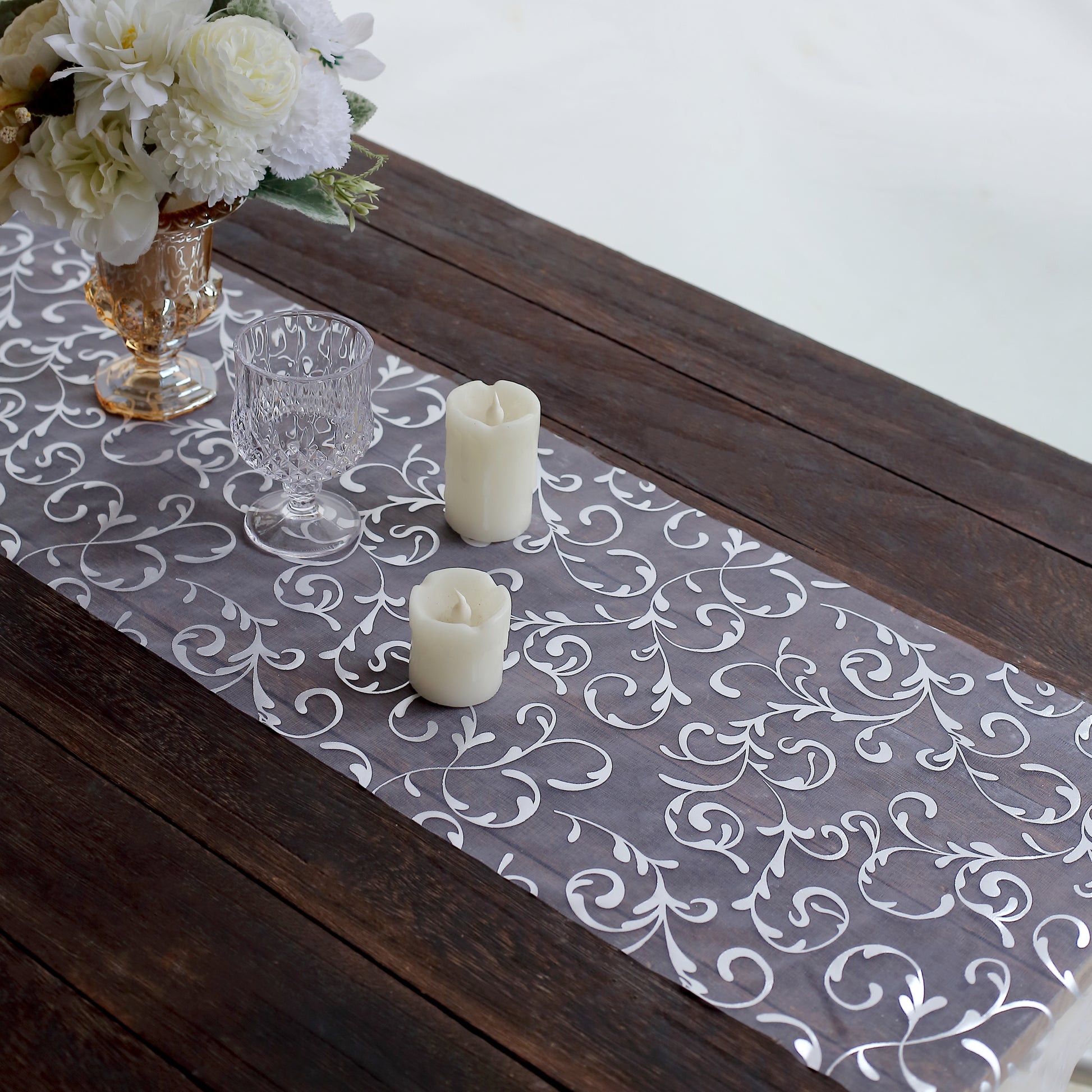 Metallic silver mesh table runner with embossed foil flower design on a wooden table.