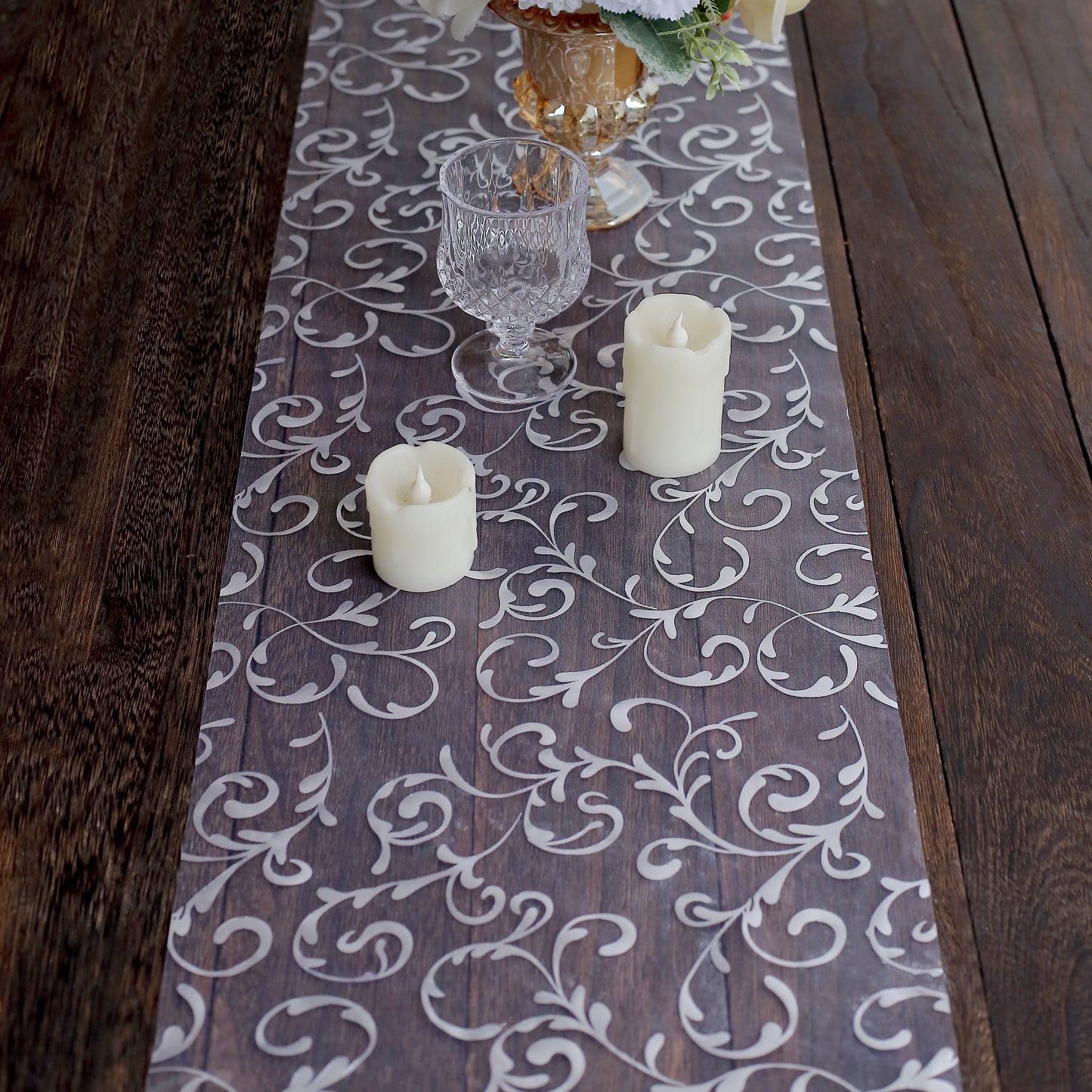 Metallic silver mesh table runner with embossed foil flower design on a wooden table.