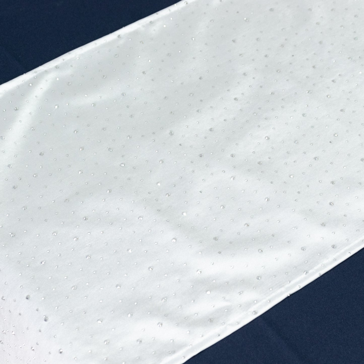 White table runner with rhinestone accents on a dark background.