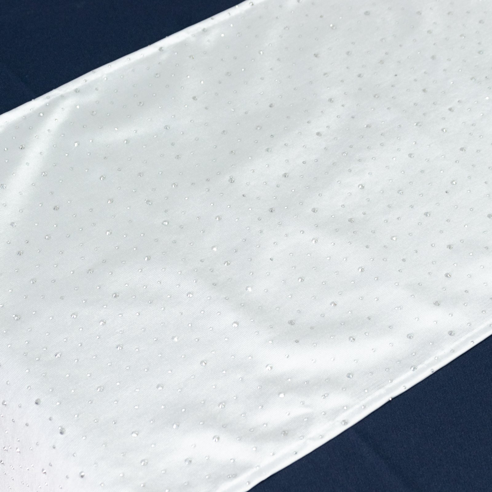 White table runner with rhinestone accents on a dark background.