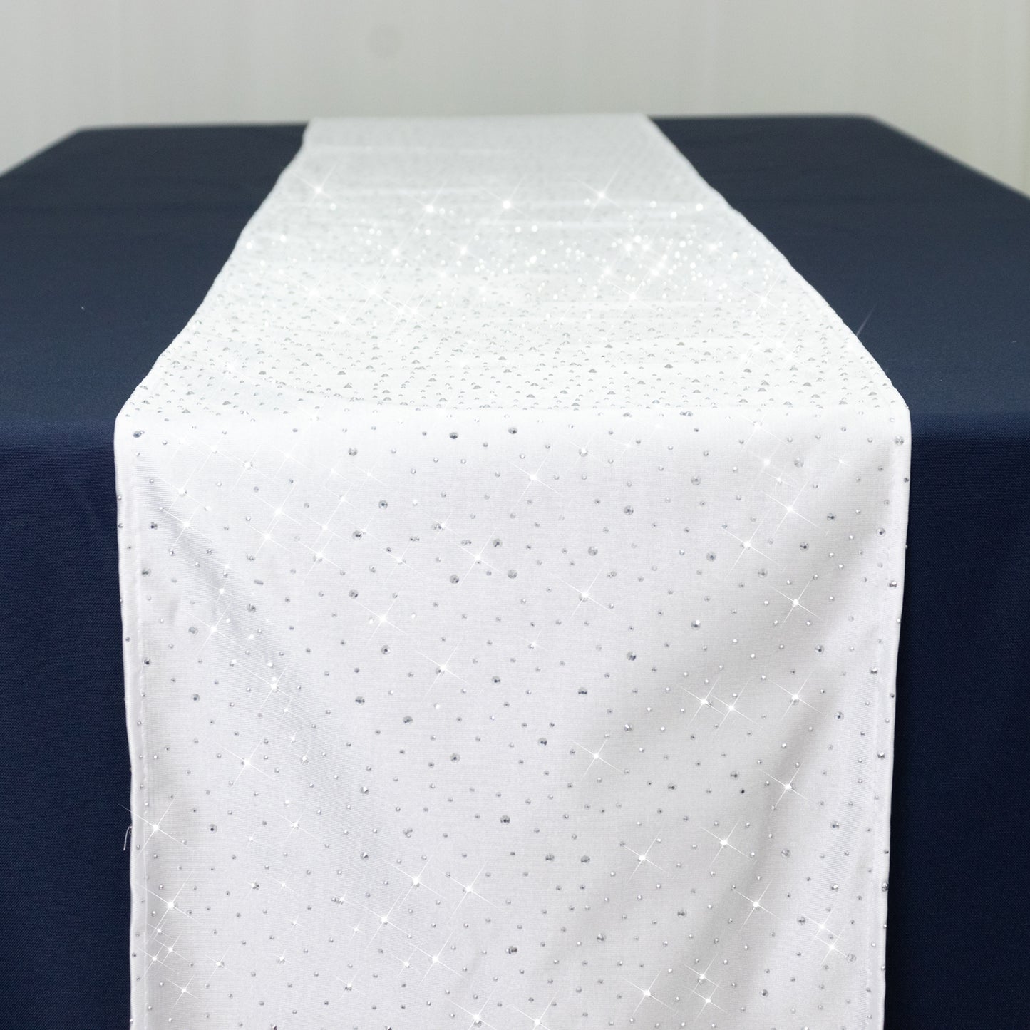 White table runner with rhinestone accents on a dark blue table.