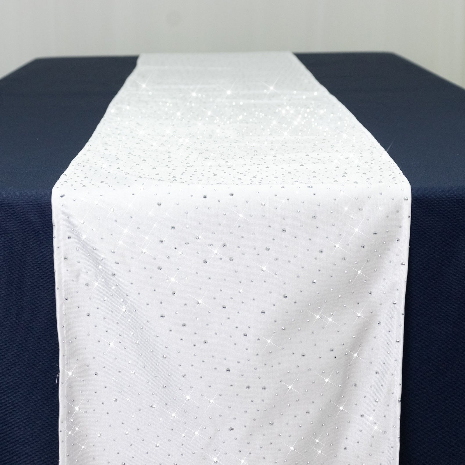 White table runner with rhinestone accents on a dark blue table.