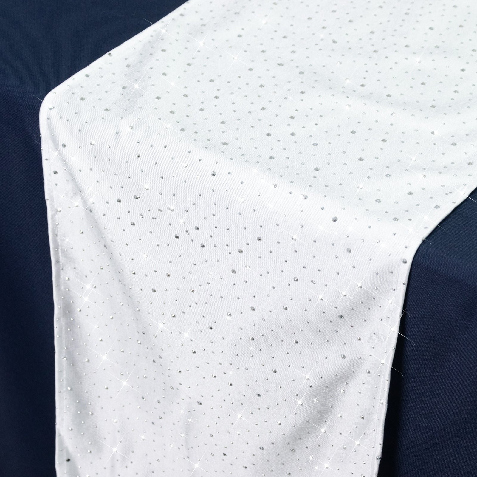 White table runner with rhinestone accents on a dark table.