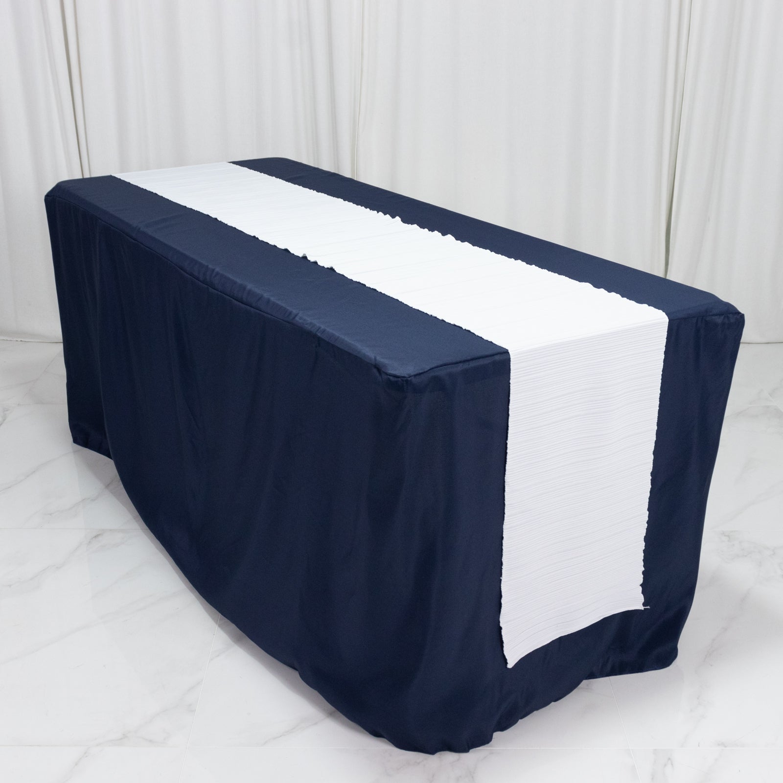 White accordion pleated table runner on a navy blue table.