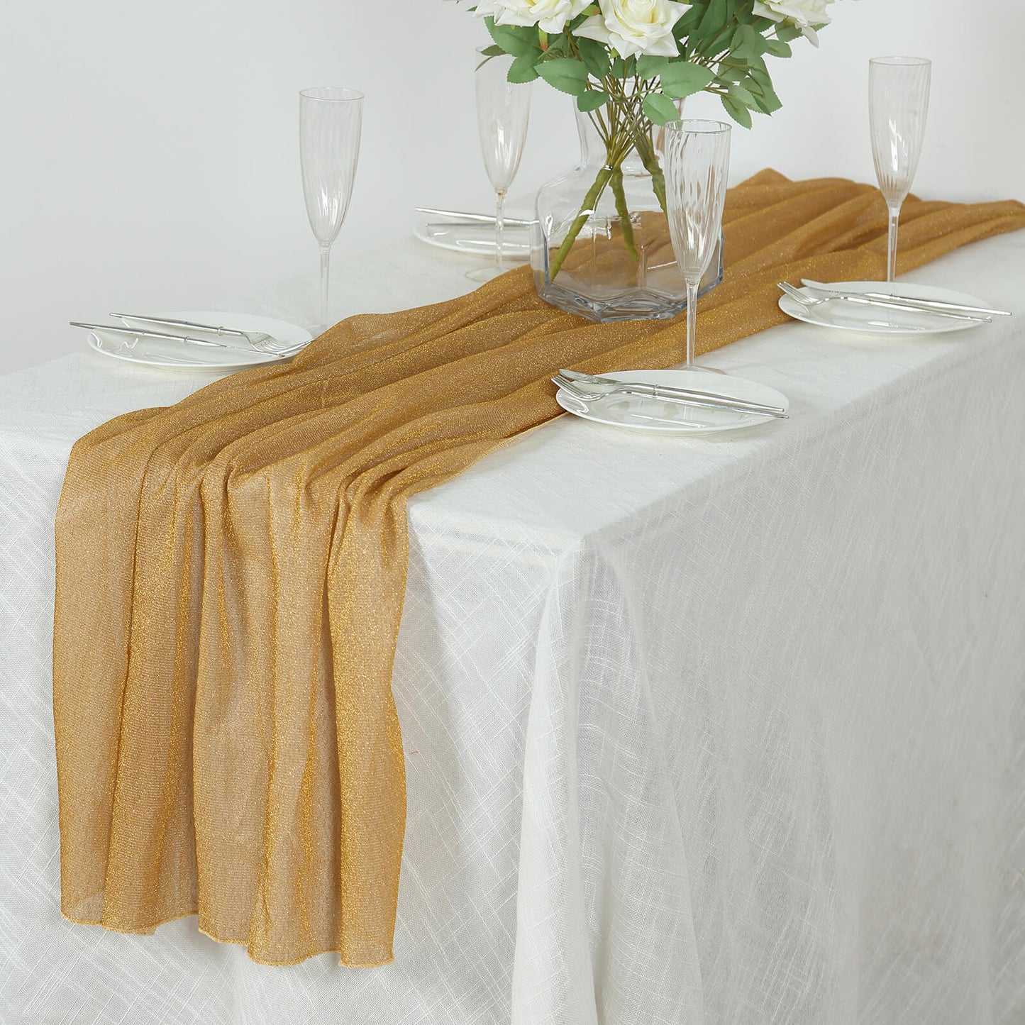 Gold sparkling glitter gauze table runner on a white tablecloth.
