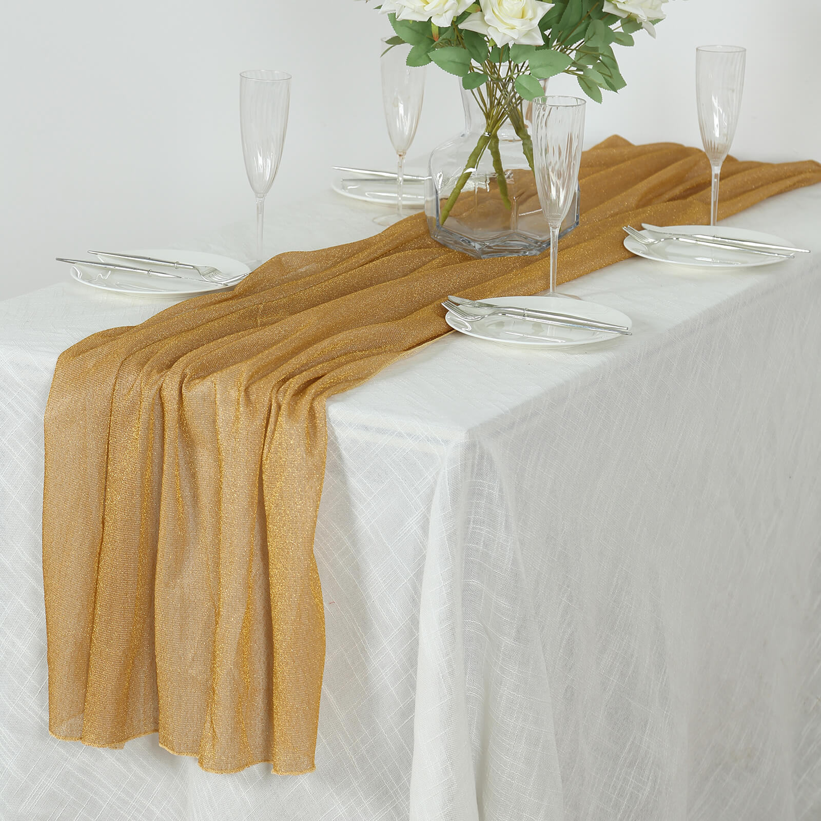 Gold sparkling glitter gauze table runner on a white tablecloth.