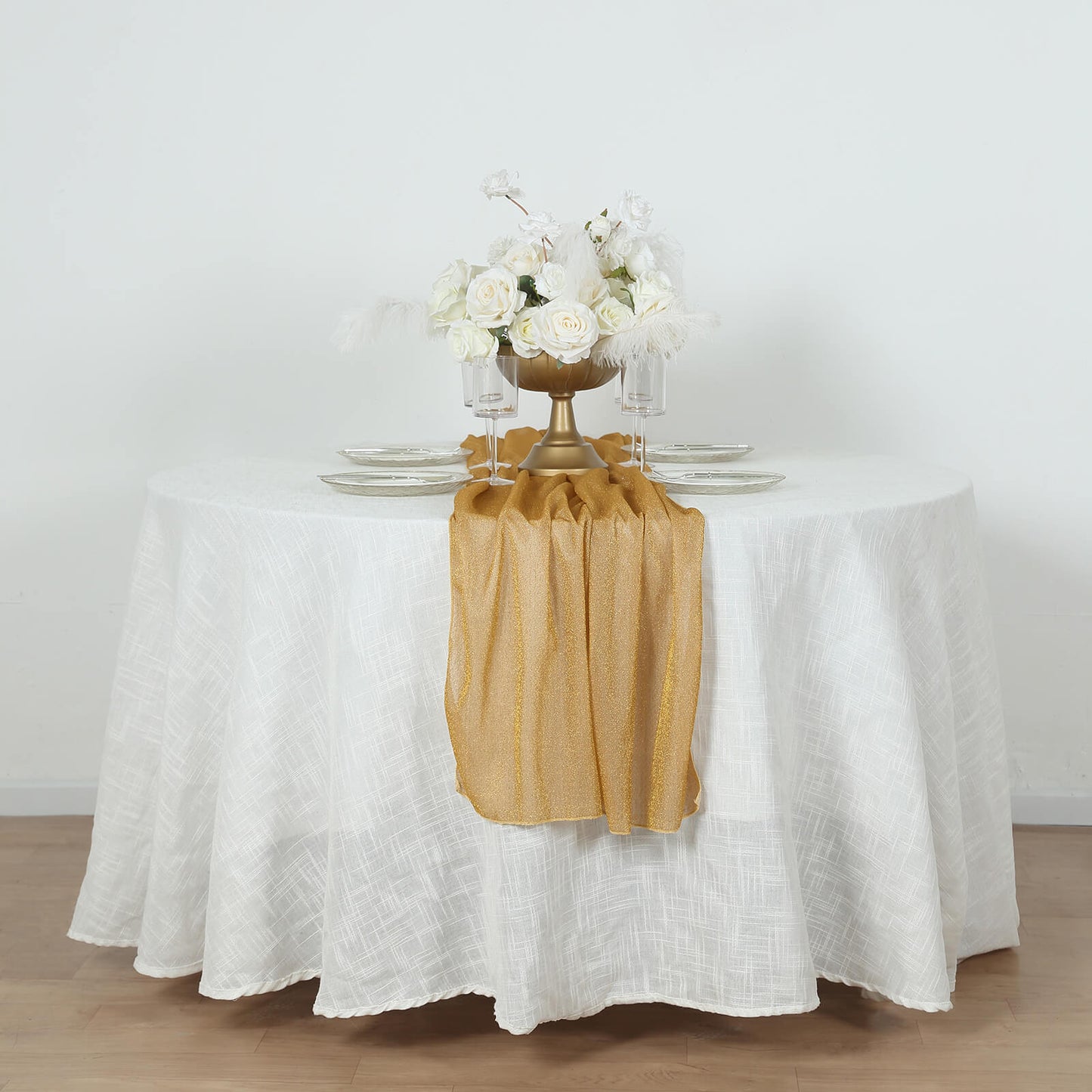 Gold glitter sheer table runner on a white table with floral arrangement.